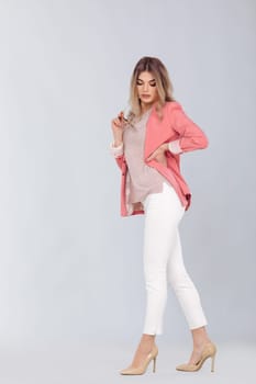 Full length portrait of attractive elegant blonde woman in pastel pink jacket posing in studio. woman dressed in trendy spring outfit