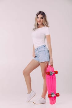 pretty woman in white t-shirt and denim shorts posing with pink skateboard