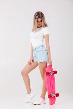 beautiful woman in white t-shirt and denim shorts with pink skateboard