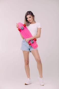 attractive woman blonde in white t-shirt and denim shorts holding pink skateboard