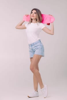 attractive woman blonde in white t-shirt and denim shorts holding pink skateboard. teenager.