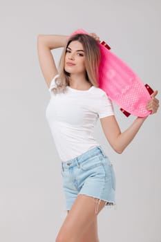 attractive woman blonde in white t-shirt and denim shorts holding pink skateboard