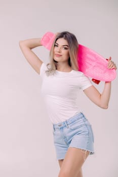 attractive woman blonde in white t-shirt and denim shorts holding pink skateboard. teenager.
