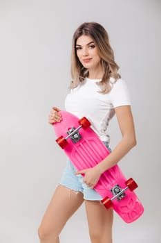 attractive smiling woman blonde in white t-shirt and denim shorts holding pink skateboard