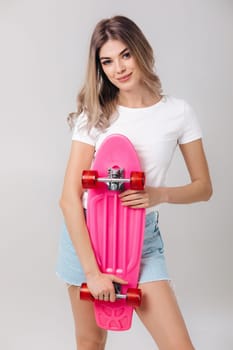 attractive woman blonde in white t-shirt and denim shorts holding pink skateboard