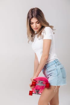 attractive woman blonde in white t-shirt and denim shorts holding pink skateboard