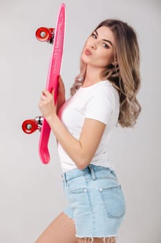 attractive woman blonde in white t-shirt and denim shorts holding pink skateboard