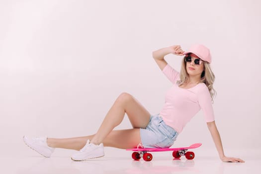 beautiful woman in sunglasses, pink t-shirt and cap sitting on pink skateboard