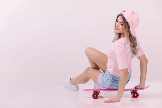 beautiful woman in pink t-shirt and cap sitting on pink skateboard