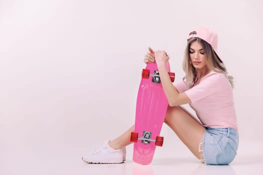 Cute woman in pink t-shirt and cap sitting on the floor with pink skateboard. teenager