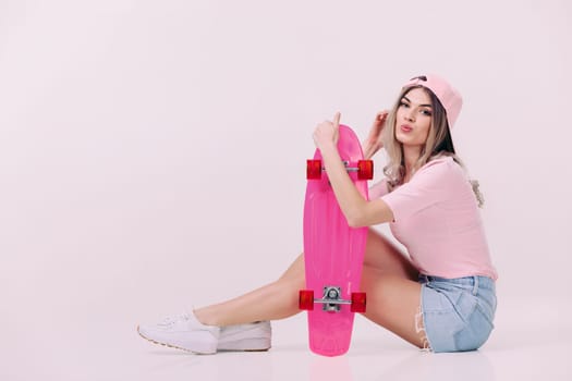 Cute woman in pink t-shirt and cap sitting on the floor with pink skateboard. teenager