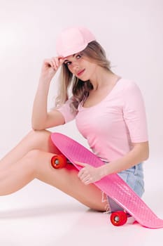 Cute woman in pink t-shirt and cap sitting on the floor with pink skateboard. teenager