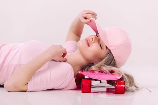 beautiful woman in pink t-shirt and cap lies on pink skateboard. relax and pleasure