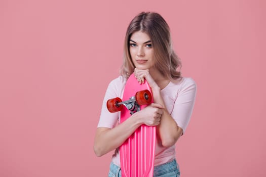 beautiful blonde woman in pink t-shirt and denim shorts hugs pink skateboard