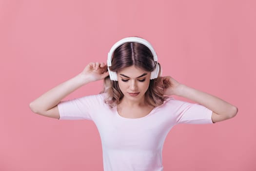 beautiful blonde woman in pink t-shirt and white headphones enjoying listens to music on pink background