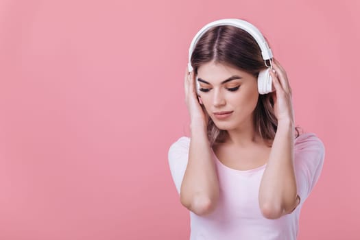 beautiful blonde woman in pink t-shirt and white headphones listens to music on pink background