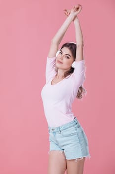 beautiful blonde woman in pink t-shirt and white headphones listens to music on pink background. summer studio photoshoot