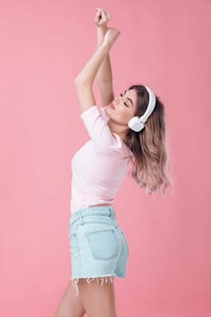 beautiful blonde woman in pink t-shirt and white headphones listens to music and dancing on pink background
