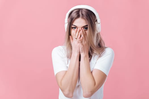 beautiful blonde woman in t-shirt and white headphones listens to music on pink background