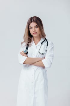 Medical physician doctor woman with crossed hands in white coat with stethoscope on light background.