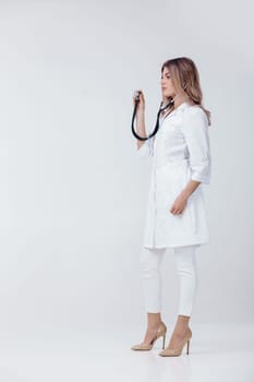 Full length portrait of medical physician doctor woman in white coat examining with stethoscope on light background.
