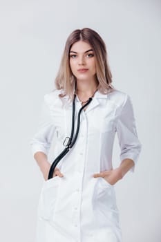 Medical physician doctor woman in white coat with stethoscope looks at camera on light background.