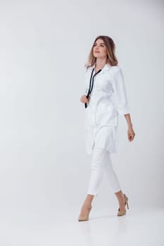 Full length portrait of medical physician doctor woman in white coat with stethoscope on light background.