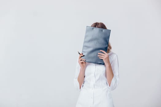 upset medical physician doctor woman in white coat covers her face with a folder.