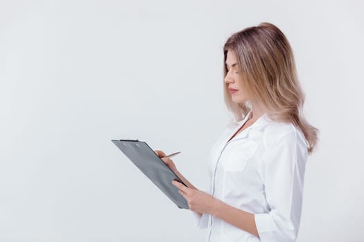 Medical physician doctor woman in white coat holding folder and filling out prescription on light background.