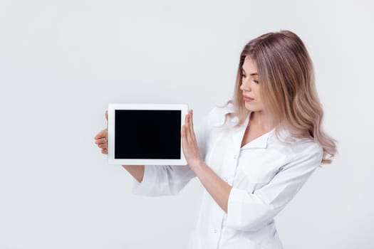 Portrait of beautiful blonde doctor in white coat showing screen of digital tablet in her hand. Healthcare and technology concept.