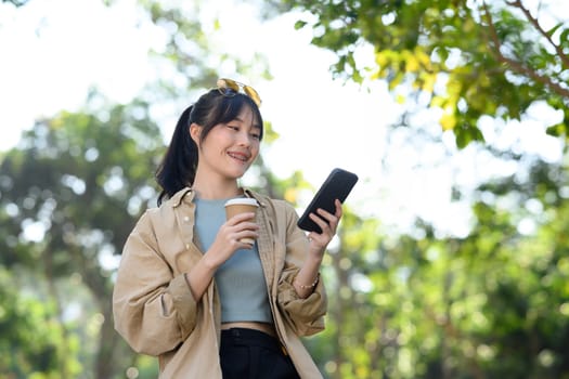 Portrait of beautiful young woman holding takeaway coffee cup and chatting on her mobile phone at outdoor.