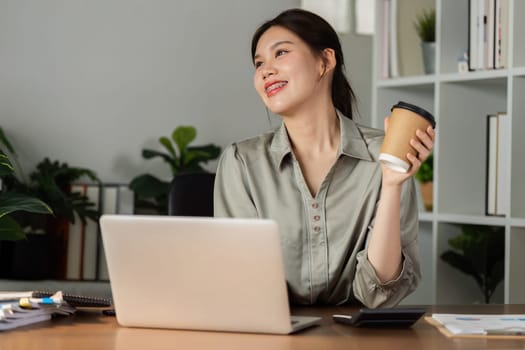 smiling businesswoman drinking coffee and working on laptop in green modern office. Nice Environment Office. Eco-Friendly Concept.