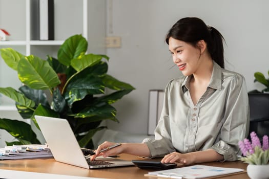 Business accountant use laptop to view company report graph and use calculator to calculate money in company report.