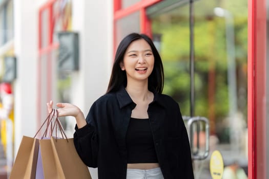 Cheerful Beautiful Asian woman holding shopping bags in shopping in the city on holiday Black Friday.