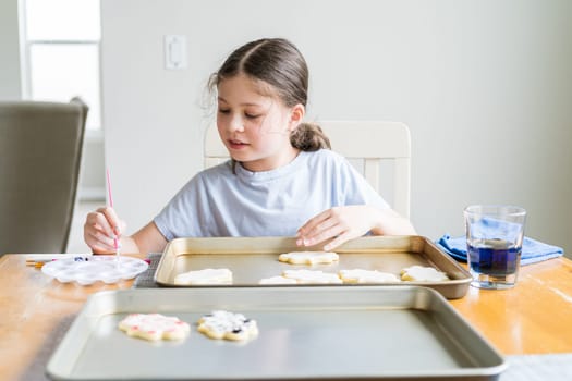 A heartwarming scene of a little girl carefully writing 'Sorry' on sugar cookies with food coloring, the cookies beautifully flooded with white royal icing.