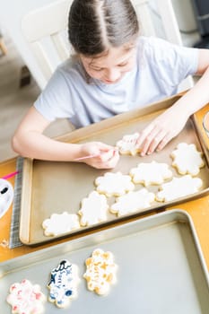 A heartwarming scene of a little girl carefully writing 'Sorry' on sugar cookies with food coloring, the cookies beautifully flooded with white royal icing.