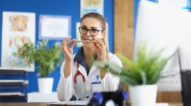 Woman doctor with glasses holding ballpoint pen in office of clinic. High quality medical consultation for patients concept