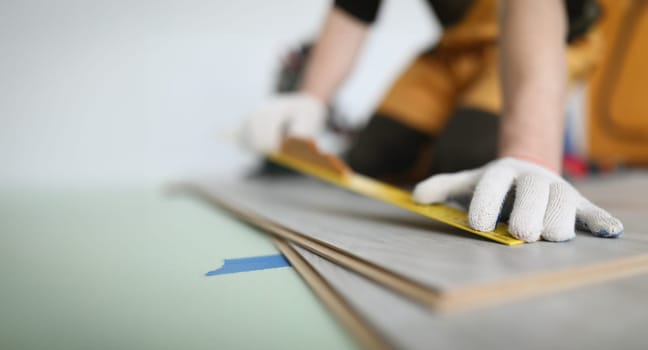 Man builder measuring laminate board with ruler for laying floor closeup. Finishing concept