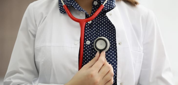 Doctor therapist holding stethoscope near his chest closeup. Heart disease diagnosis and treatment concept