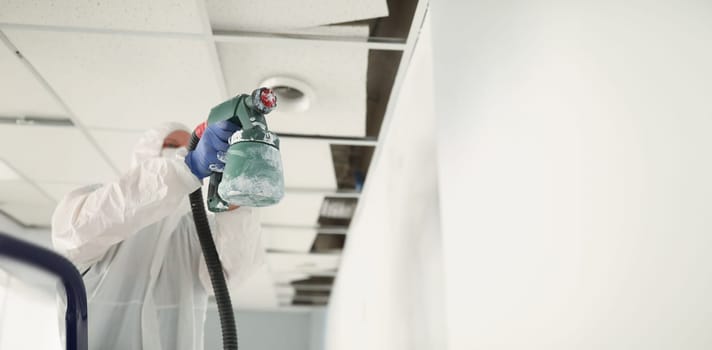 Male construction worker in protective overalls painting wall white with spray gun closeup. Finishing of apartments concept