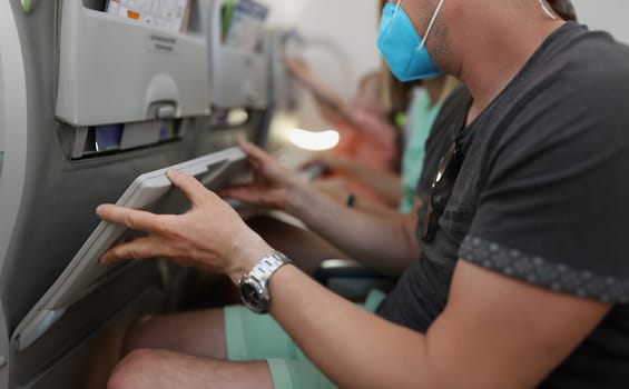 Man in protective medical mask lifting table on airplane seat closeup. Rules of conduct on airplane during pandemic covid19 concept