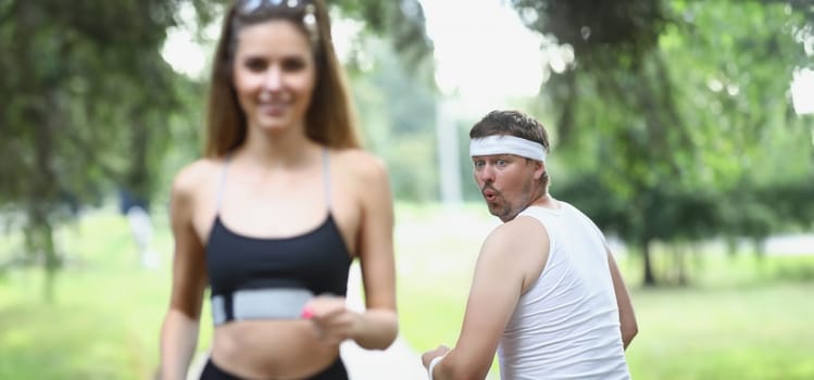 Fat man looking at young woman athlete jogging in park. Morning jogging healthy lifestyle concept