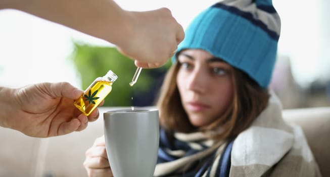 Drops of marijuana oil dripping into cup of sick woman wearing hat closeup. Cannabis addiction concept