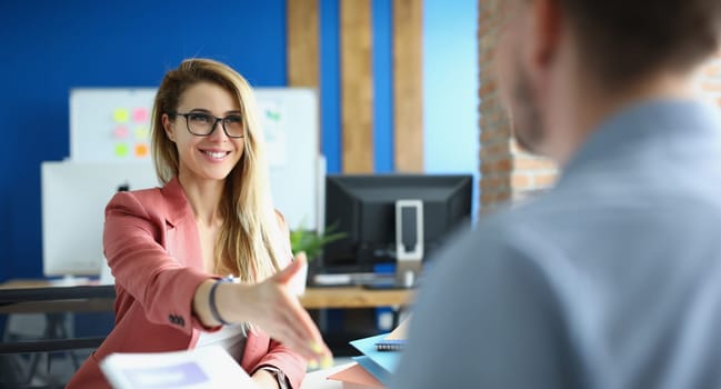 Businesswoman with glasses giving her hand for handshake to her partner. Teamwork concept