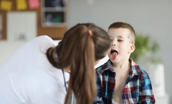 Doctor pediatrician examining throat of little boy in clinic. Treatment of seasonal colds in children concept