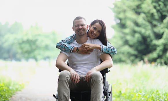 Woman hugging man in wheelchair in park portrait. Close relationship with disabled people concept