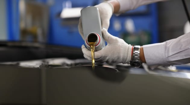 Master repairman pouring engine oil under hood of car closeup. Motor oil change interval concept