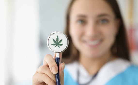Doctor holding stethoscope with drawn marijuana leaf closeup. Narcotic drug treatment concept