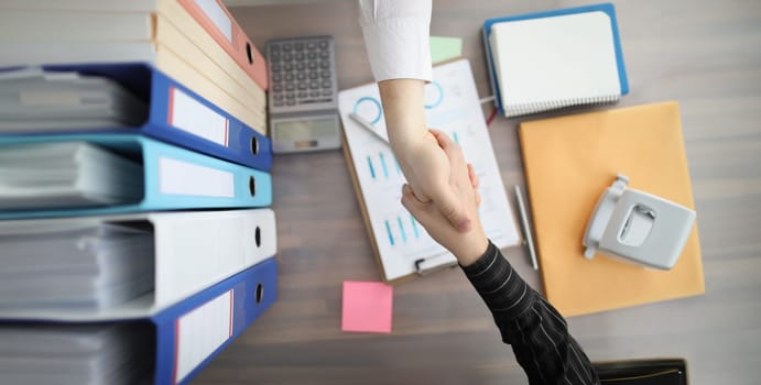 Closeup of handshake of business people on background of documents and folders on table top view. Successful partnership work in business concept