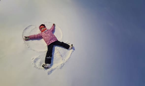 Little girl lying in snow and making angel top view. Children winter fun concept